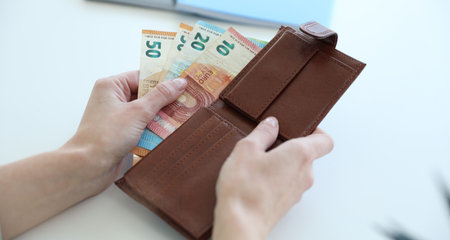Woman putting euro banknotes into wallet at white table, closeup