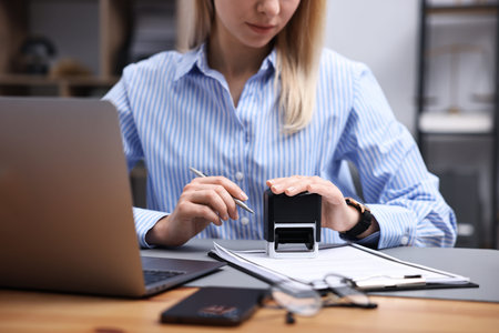 Notary stamping document at wooden desk in office, closeup