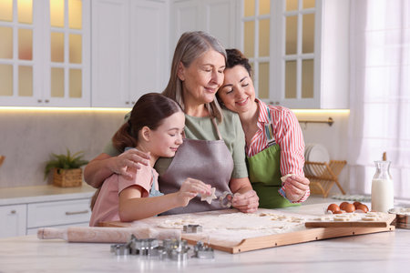 Smiling grandmother, her daughter and granddaughter cooking together at white marble table in...