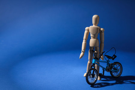 Wooden mannequin with toy bicycle on blue background, space for textの写真素材