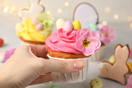 Woman tasty taking decorated Easter cupcake and festive decor at table, closeup
