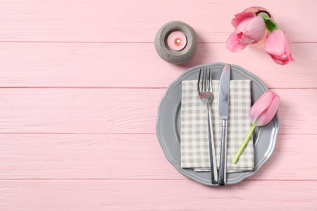 Stylish table setting with floral decor and burning candle on pink wooden background, flat lay....