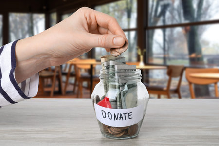 Woman putting coins into jar on table in cafe, closeup