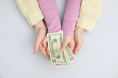 Alimony. Mother and daughter with dollar banknotes on light gray background, top view