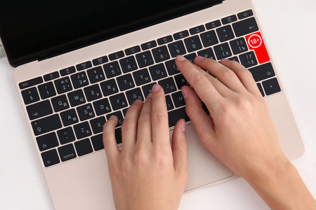 Woman using laptop with red button 18 plus at table, top view. Adult content warning