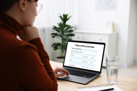 Visa application. Woman using laptop to fill in online form at table, closeupの写真素材