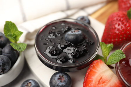 Sweet jam in glass bowl, strawberries, blueberries and mint on table, closeup