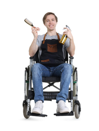 Smiling hairdresser wearing apron with spray bottle and comb in wheelchair on white backgroundの写真素材