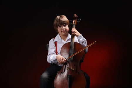 Little boy playing violoncello on dark red background