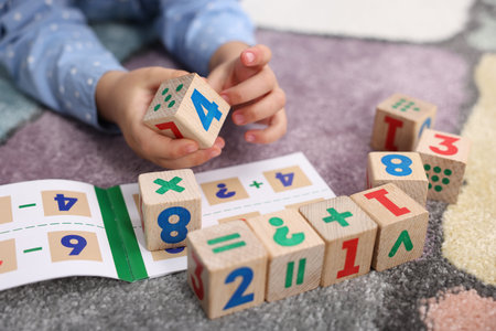 Little girl playing with wooden cubes on colorful carpet, closeup. Educational toyの写真素材