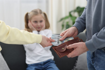 Alimony. Man giving money to ex-wife while his sad daughter sitting on sofa at home, selective focus