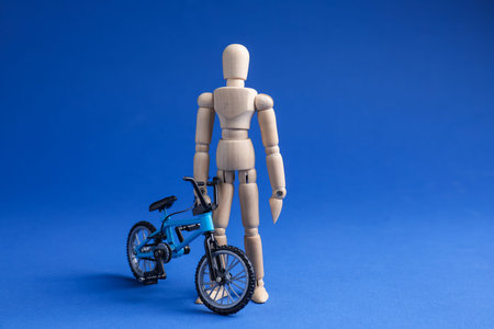 Wooden mannequin with toy bicycle on blue background, space for textの写真素材