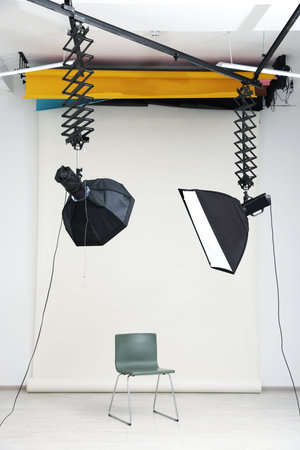 Professional lighting equipment hanging from ceiling and chair in photo studioの写真素材