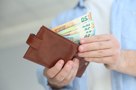 Man putting euro banknotes into wallet against blurred background, closeup