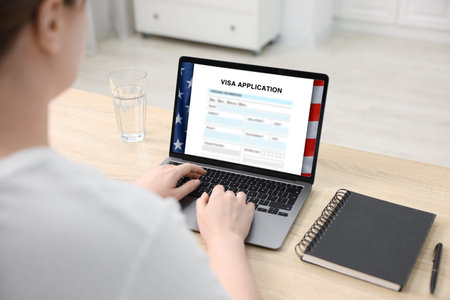 Woman using laptop to fill in online visa application form at table, closeup