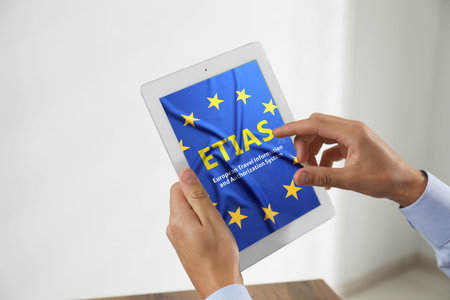 Man viewing ETIAS webpage using tablet computer indoors, closeup. European Travel Information and...