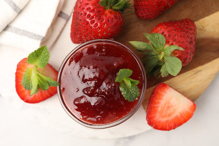 Sweet jam in glass bowl, strawberries and mint on white marble table, top view