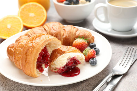 Yummy breakfast. Tasty croissants with jam, berries and coffee on light grey table, closeup