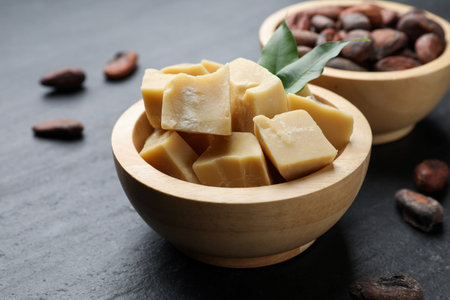 Cocoa butter, beans and green leaves on black table, closeup