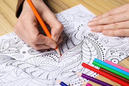 Woman coloring antistress picture with pencils at wooden table, closeupの写真素材