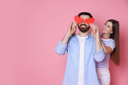 Romantic date. Lovely couple with red paper hearts on pink background, space for textの写真素材