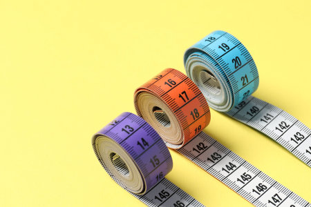 Different measuring tapes on yellow background, closeup. Space for text