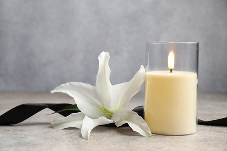 Beautiful LED candle, white lily and black ribbon on light grey table, closeupの写真素材