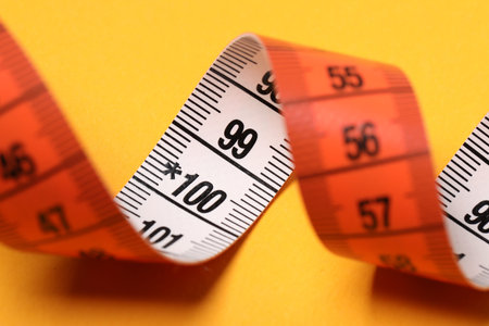 One measuring tape on orange background, closeup