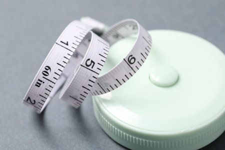 One measuring tape on grey background, closeup