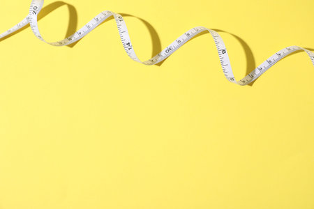 One measuring tape on yellow background, top view. Space for text