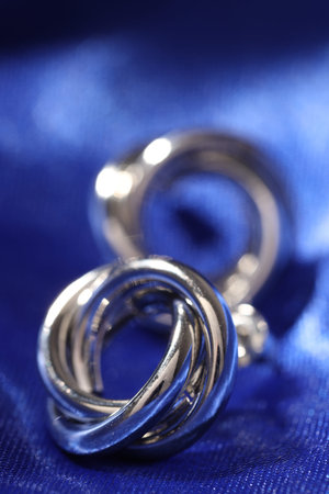 Shiny silver earrings on blue silk cloth, closeup