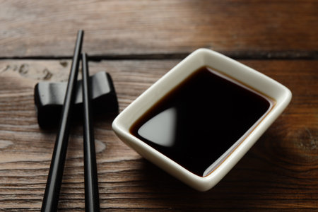 Soy sauce in bowl and chopsticks on wooden table, closeupの写真素材