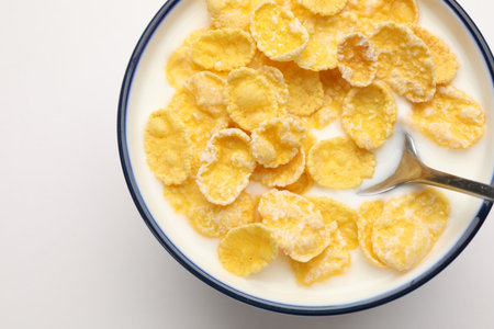 Tasty corn flakes with milk in bowl served on white table, top view