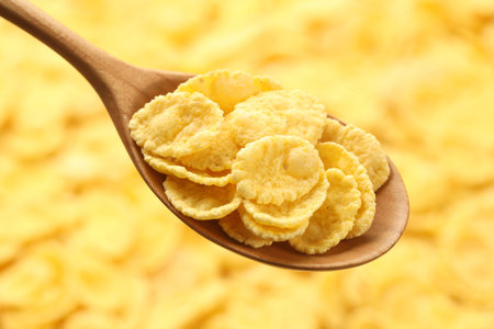 Spoon with corn flakes and milk against blurred yellow background, closeup