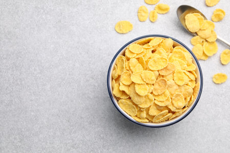 Tasty corn flakes in bowl and spoon on light grey table, flat lay. Space for text
