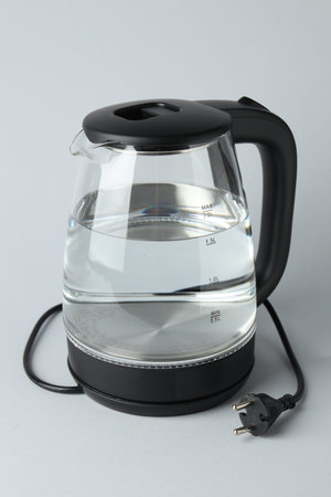 Modern electric kettle with water on light grey background