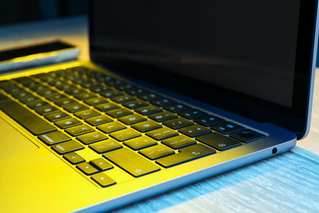 Modern laptop in neon lights on wooden table, closeup