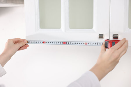 Woman measuring cabinet with tape in kitchen, closeup