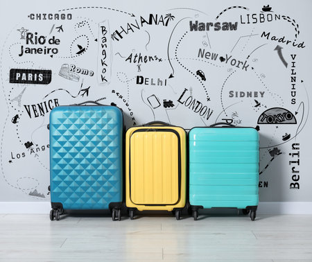Journey planning. Suitcases against drawing of cities to visit and symbols for travel methods on grey wallの写真素材