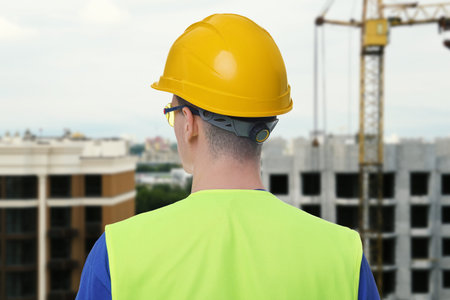 Builder in workwear and hard hat at construction site, back view