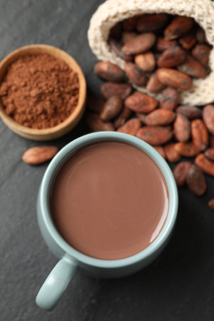 Yummy cocoa in cup, beans and powder on dark grey table, flat lay