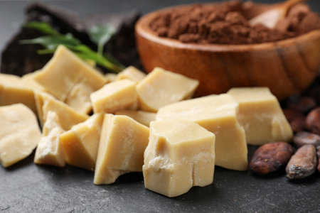 Cocoa butter, beans, powder and green leaves on black table, closeup