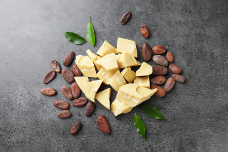 Organic cocoa butter, beans and green leaves on grey table, flat lay
