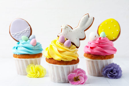 Tasty decorated Easter cupcakes and flowers on white tiled table, closeup