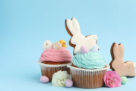Tasty cupcakes with Easter decor on light blue background, closeup. Space for text