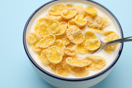 Tasty corn flakes with milk in bowl served on light blue table, closeup