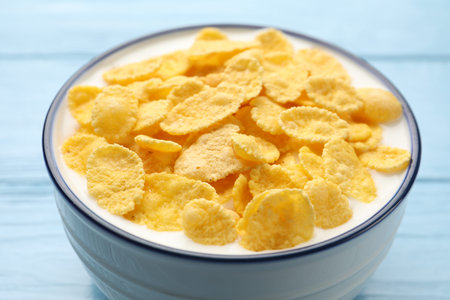 Tasty corn flakes with milk in bowl on light blue wooden table, closeup
