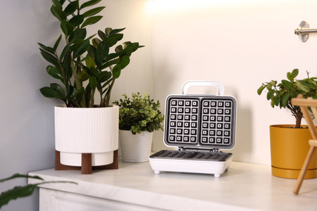Potted houseplants and waffle maker on countertop in kitchen, closeup. Interior design