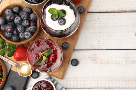Tasty yogurt with berries, jam and mint on white wooden table, flat lay. Space for text