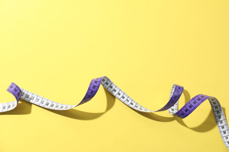 One measuring tape on yellow background, top view